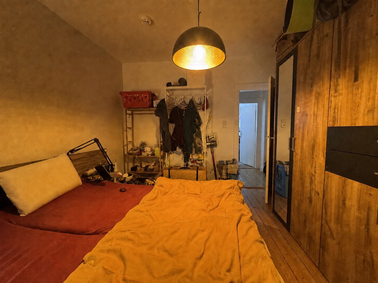 Schlafzimmer aus der Gegenperspektive mit Bett, Kleiderschrank und Kleiderständer