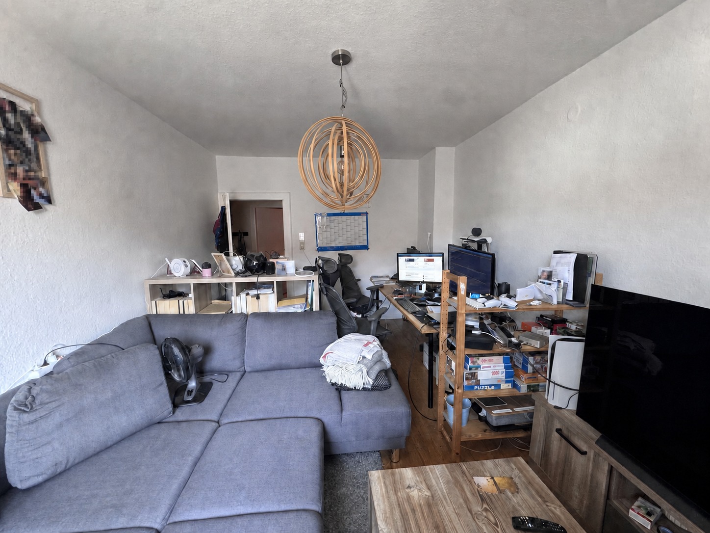 Wohn- und Arbeitszimmer mit grauem Sofa, Schreibtisch und Fernseher